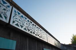 A low angle shot of the Sea to Sky mural, made of five identical steel panels with carvings that reveal blue and green stained glass behind them, with a light blue sky in the background.