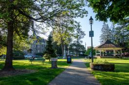 A concrete pathway leading to Sylvester Park, which features open lawns, park benches, trees, a statue, and a gazebo, as well as an amazing view of the Old Capitol Building in the background.