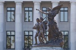 A side profile of the Winged Victory Monument, which is made of granite a base with five bronze figures atop it: the famous Greek statue of Nike of Samothrace; a U.S. sailor, soldier, marine; and a Red Cross nurse.