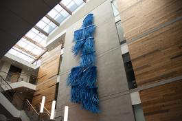 A low angle view of the Hydro Logic, a large, blue aluminum sculpture hanging on a wall above a stairway inside of the Helen Sommers building.