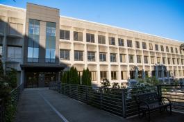 A concrete path with metal railings leading to the upper entrance of Office Building 2, located on the northwest side of the building. Green trees on the level below this pathway are showing on both sides of it, and there is a metal bench on the right side of the path.