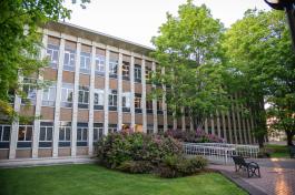 A view of the Employment Security Department Building entrance from the southwest. The three-story building is made of white and brown stone, and the walkway leading to the entrance is lined with green trees and flowering bushes. 