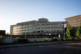 A wide shot of the Natural Resources Building, one of the largest buildings on Capitol Campus, which is predominantly made of concrete. The Natural Resources Building parking garage is in the foreground and the Highways-Licenses Building is in the background, with various trees and other plants scattered between the areas.