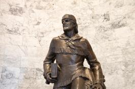 The Marcus Whitman statue from the waist up, which shows Whitman holding a thick book and multiple satchels. This depiction of Whitman wears a shirt with tassels on the chest, waist, and forearm areas.
