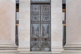 A set of bronze doors at the front of the Legislative Building. The dark bronze has some blueish green spots due to weathering but remains in overall good condition.