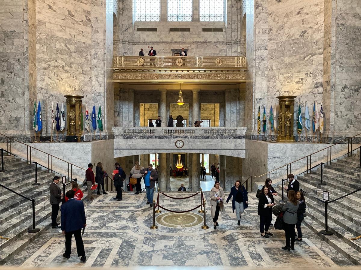 People walking around and taking photos of the Legislative Building's interior, which is primarily marble with gold accents.