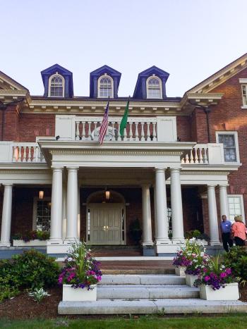 The front side of the Governor's Mansion, which is made of red bricks and white accents. An American flag and Washington State flag hang above the front porch.