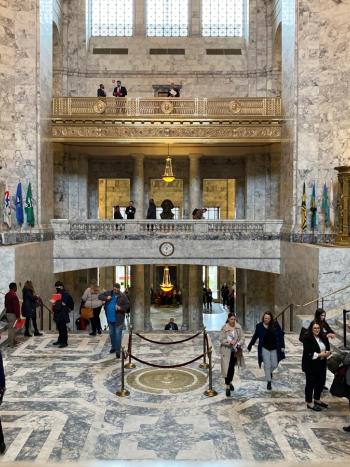 People walking around and taking photos of the Legislative Building's interior, which is primarily marble with gold accents.