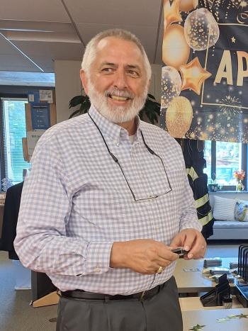Bob Whitney, an elderly man, smiles for a photo in front of a banner that says "We appreciate you" after receiving an award for his 20 years of public service.