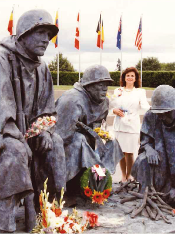 A photo of Ms. Fellows, dressed in a white suit, standing with her sculpture commemorating the Korean War.