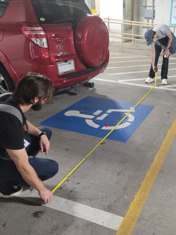 2 DES staff employees measuring the width of an ADA parking spot with a measuring tape.