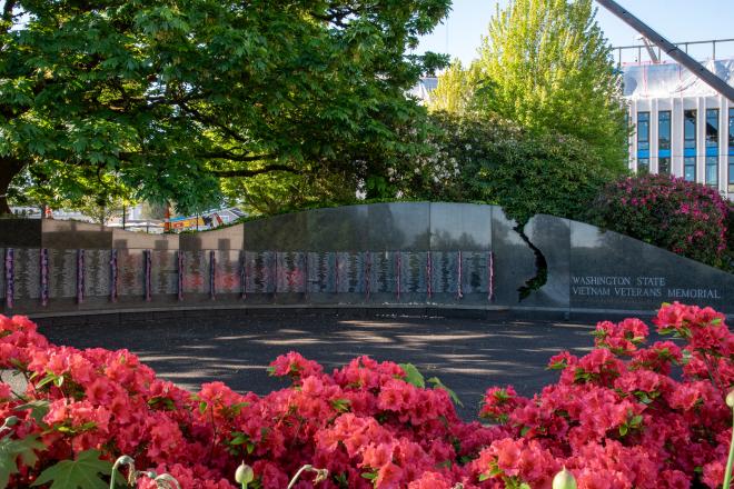 The Vietnam War Memorial with red flowers in the foreground and trees in the background.