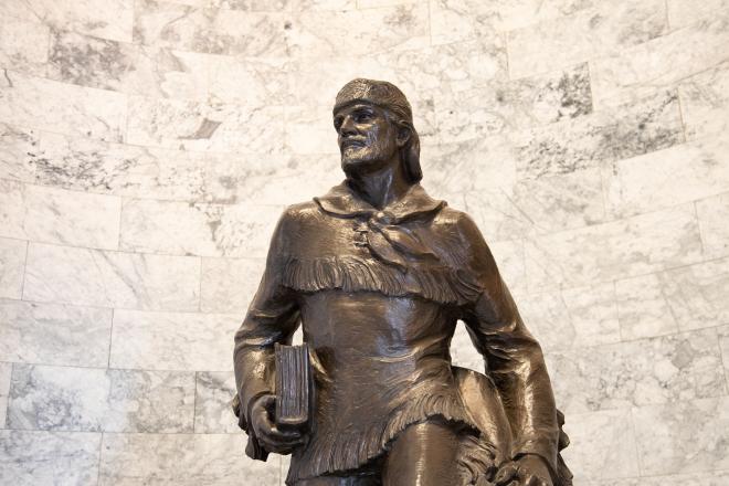 The Marcus Whitman statue from the waist up, which shows Whitman holding a thick book and multiple satchels. This depiction of Whitman wears a shirt with tassels on the chest, waist, and forearm areas.